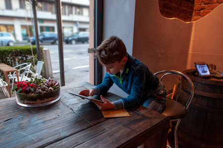 young boy using a tablet sitting in a pub in front of a large window - addicted generation conceptの写真素材