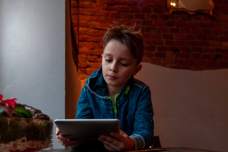 young boy using a tablet sitting in a pub in front of a large window - addicted generation conceptの写真素材