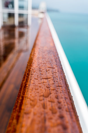 close up of raindrops on a wooden handrail on the deck of a ship on a cloudy dayの写真素材