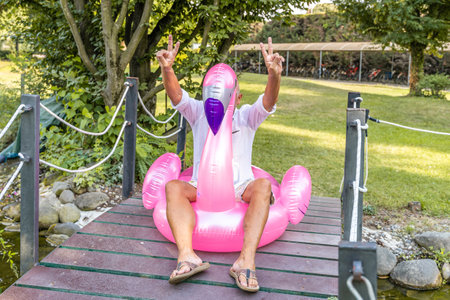 Smiling handsome middle aged man having fun sitting on an inflatable pink flamingo toy