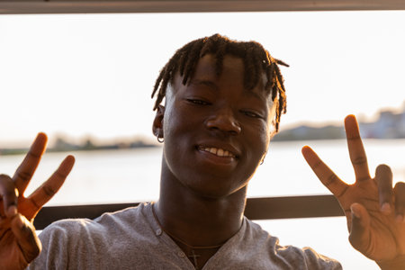 portrait of young handsome african american man sitting on boat sailing during summer vacation on a riverの写真素材