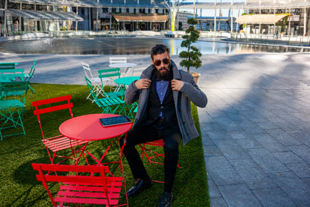 young hipster businessman consults his laptop sitting outdoors in a small urban park