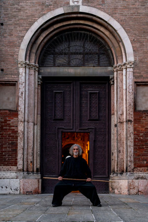 Middle-aged tai chi master showing stick exercises outdoors amidst the architecture of a medieval buildingの写真素材