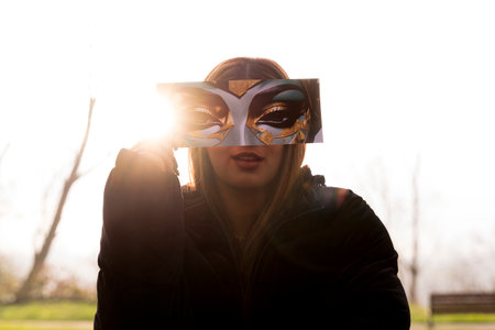 portrait of young woman having fun showing a fantasy image partially covering their face in a public park in winterの写真素材