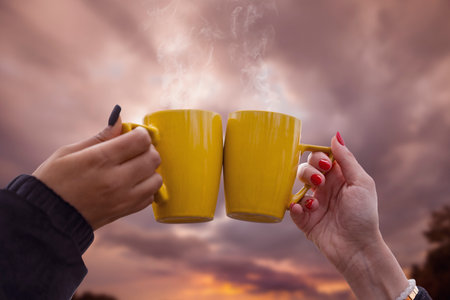closeup of a toast between two yellow cups held aloft by two female hands with well-manicured nails