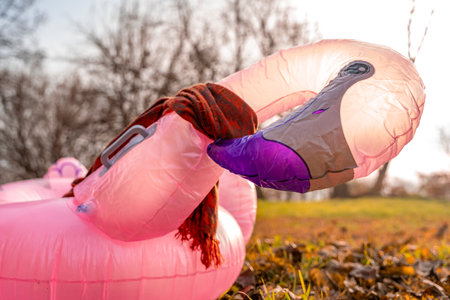 an inflatable life preserver in the shape of a pink flamingo with a red scarf around its neck among fallen leaves on a meadow in autumnの写真素材