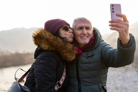 beautiful happy middle aged couple in love in winter clothes taking a selfie outdoors on a windy dayの写真素材
