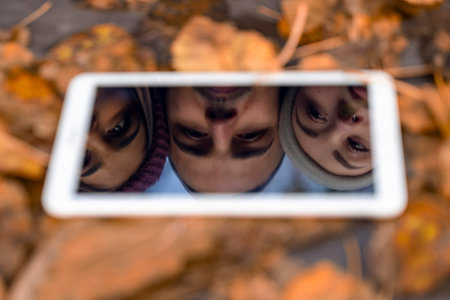 three friendly faces male and female reflecting on the screen of a tablet leaves among a multitude of autumn leavesの写真素材