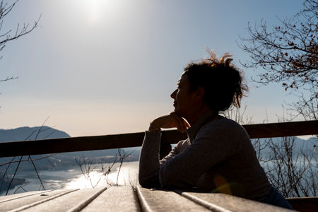 middle aged woman looking at the view sitting at a wooden table on a path by the lakeの写真素材