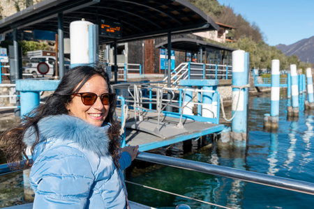 beautiful smiling woman in winter clothes docking with ferry at a small tourist port on an Italian lakeの写真素材