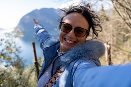 happy middle aged woman taking a selfie surrounded by nature in front of a beautiful top view of the lakeの写真素材