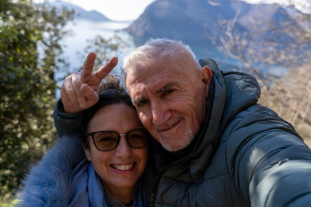 beautiful middle aged couple in love taking a selfie surrounded by nature in front of a lake viewの写真素材