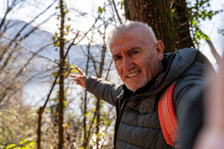 happy middle aged man taking a selfie surrounded by nature in front of a beautiful top view of the lakeの写真素材