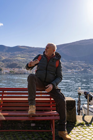 middle aged man taking a selfie sitting on a bench by an Italian lakeの写真素材