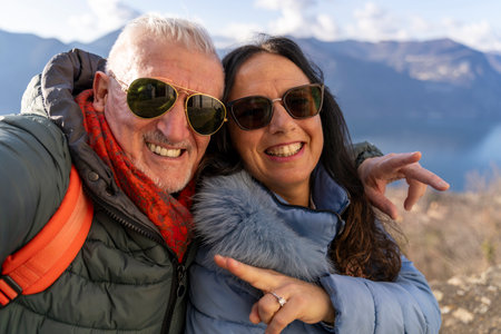 beautiful middle aged couple in love taking a selfie surrounded by nature in front of a lake viewの写真素材