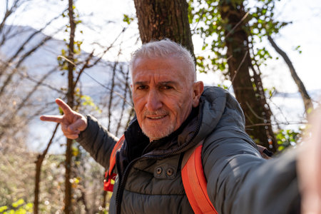 happy middle aged man taking a selfie surrounded by nature in front of a beautiful top view of the lakeの写真素材