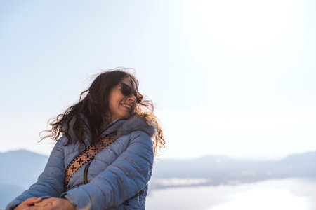 happy middle aged woman wearing sunglasses posing surrounded by nature in front of a beautiful top...
