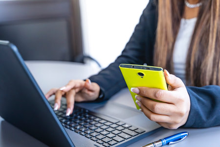 young business woman working typing on laptop keyboard and talking on mobile phone in modern officeの写真素材