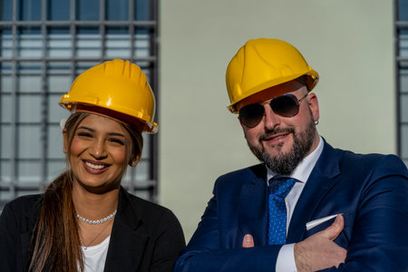 portrait of two young smiling business people male and female working outdoors wearing yellow safety helmetの写真素材