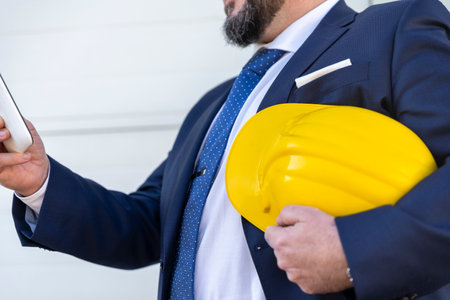 bottom up portrait of bearded businessman working outdoors using tablet wearing yellow protective helmet and transparent work glassesの写真素材