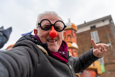 handsome middle aged man taking a selfie wearing a funny mask posing during a carnival parade in the streetの写真素材