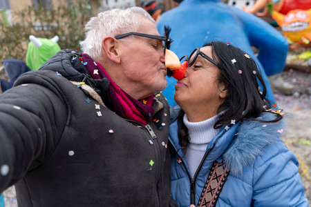 masked middle aged couple taking a selfie kissing under a shower of confetti during a carnival parade in the streetの写真素材