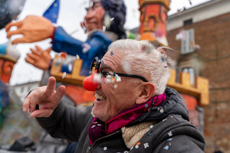 handsome middle aged man taking a selfie wearing a funny mask posing during a carnival parade in the streetの写真素材