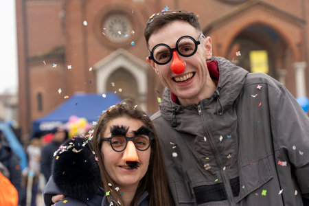 portrait of young adult couple having fun with masks and confetti during a carnival parade in front of a churchの写真素材