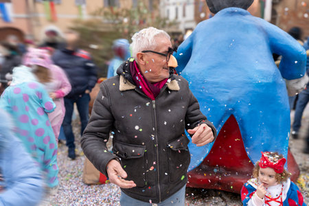 handsome middle aged man taking a selfie wearing a funny mask posing during a carnival parade in the streetの写真素材