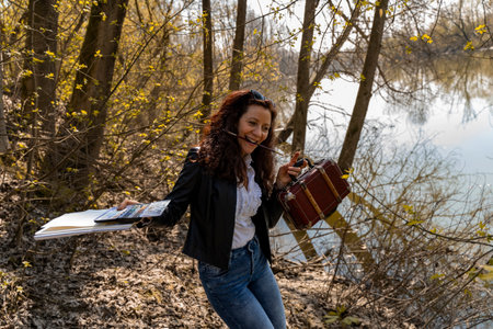 red-haired female artist with watercolor painting equipment on a river bankの写真素材