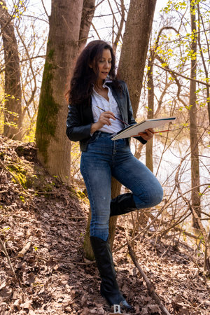 attractive red-haired female artist painting with watercolors on a river bankの写真素材