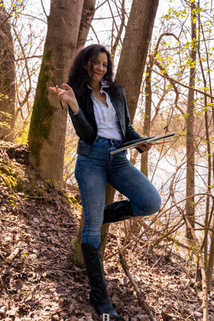 attractive red-haired female artist with watercolor painting equipment on a river bankの写真素材