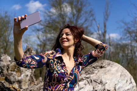 attractive smiling red-haired woman taking a funny selfie sitting on a big log outdoorsの写真素材