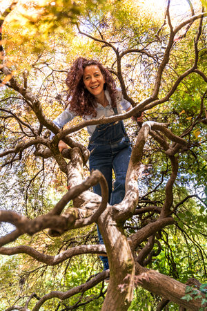 beautiful smiling woman with red hair climbing on the twisted branches of a holm oak treeの写真素材
