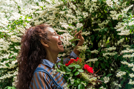 portrait of beautiful smiling woman with red hair holding a bunch of colorful flowers smelling the white flowers surrounding herの写真素材