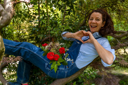 beautiful smiling woman with red hair lying on the branches of a tree showing the heart symbol with her handsの写真素材