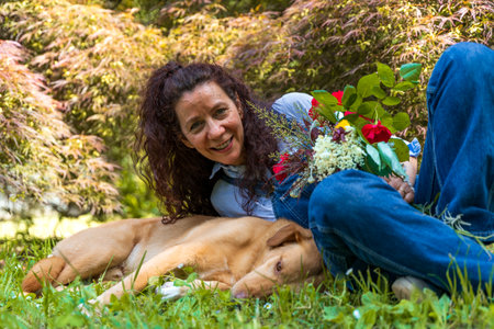 middle aged woman enjoying happy moments with her dog lying in the grass of a parkの写真素材