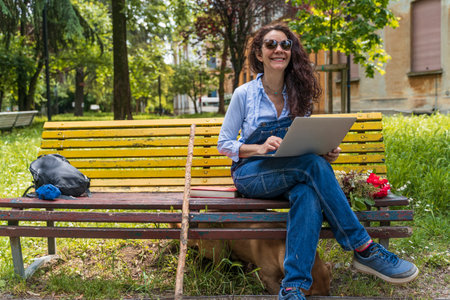 middle aged woman in casual clothes sitting on yellow bench using laptopの写真素材