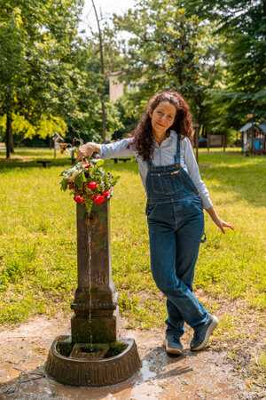 woman with red hair showing a bouquet of flowers standing near a public fountain in a city parkの写真素材