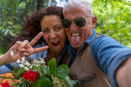 beautiful and harmonious middle-aged couple smiling and taking funny selfie making peace sign with hand outdoorsの写真素材