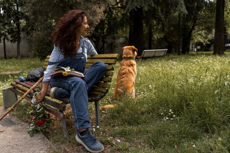 woman with red hair sitting on a yellow bench relaxing with her dog in a city parkの写真素材