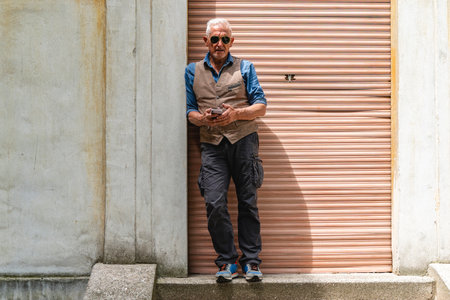 elegant middle-aged man wearing sunglasses using mobile phone standing on concrete staircase outdoorsの写真素材