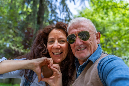 beautiful middle aged couple taking selfie showing heart symbol with hand outdoorsの写真素材