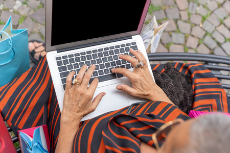 close up of mature woman's hands typing on laptop keys on metal benchの写真素材