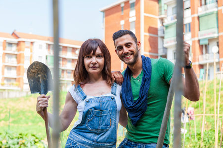 Couple smiling, holding gardening tools working together in a community gardenの写真素材