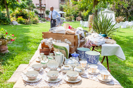 Vintage porcelain tea sets and other household items displayed on a table outdoors for saleの写真素材
