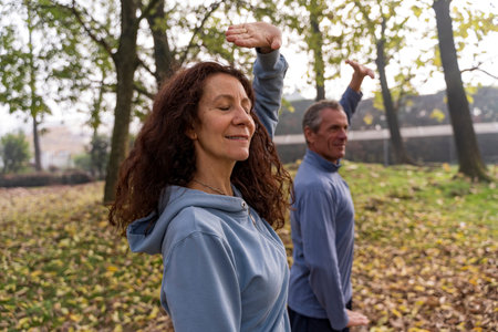 Senior couple performing exercises outdoors in park, focusing on wellness and mindfulness