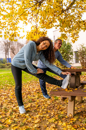Mature couple warming up with leg stretches in a park covered with fallen yellow leaves