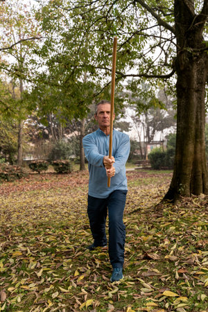 Senior man focusing on martial arts training with a bo staff outdoors