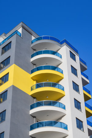 The upper part of a tall residential building with semicircular balconies against a blue sky.の写真素材